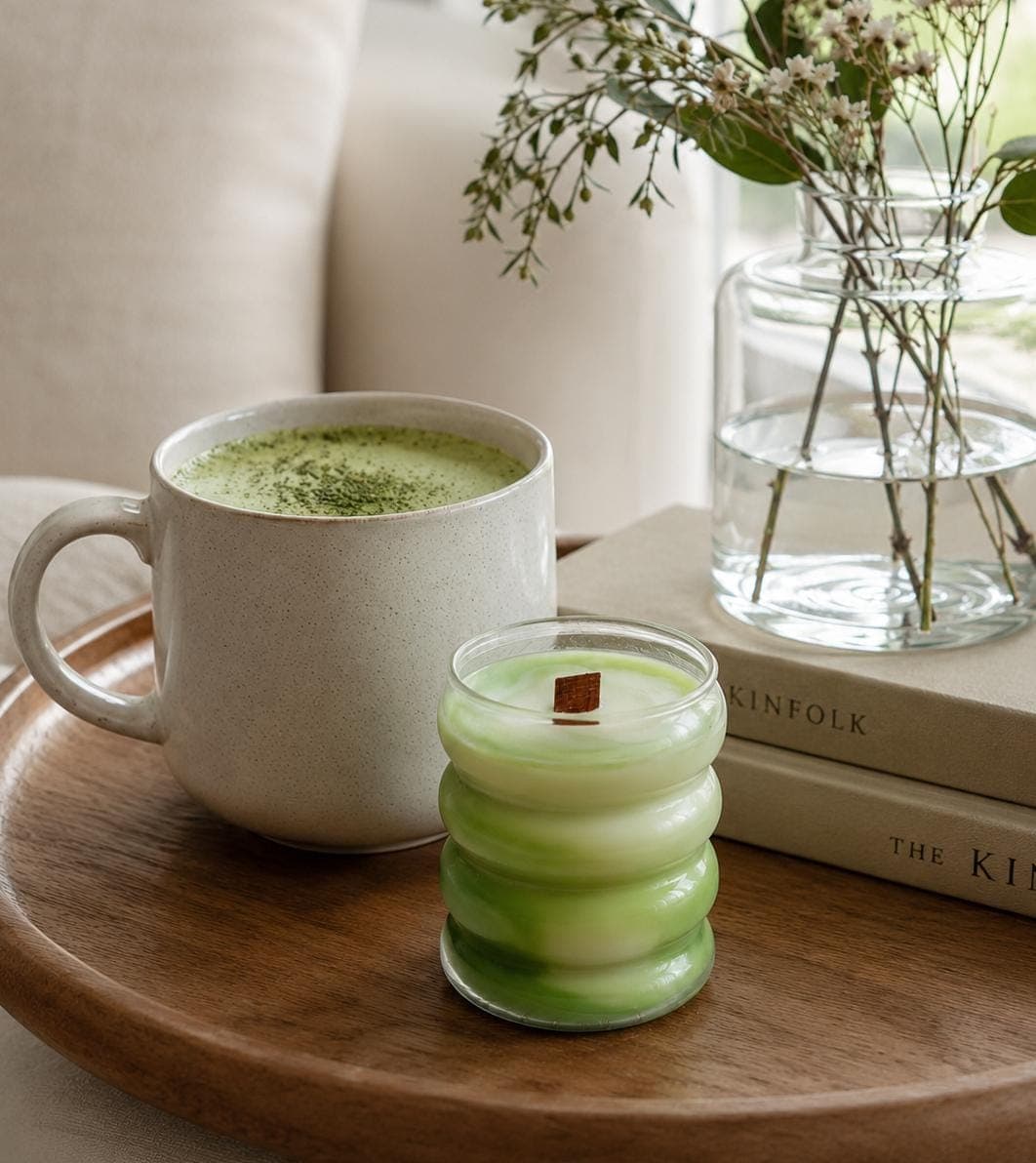Vela Melon Matcha Latte sobre una bandeja de madera junto a una taza grande de matcha latte y un par de libros